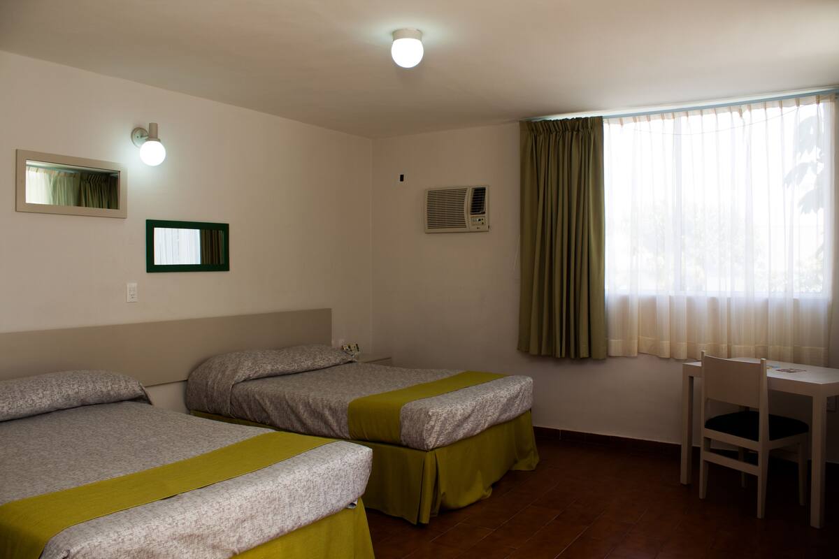 A room with two beds, a desk, and a window with curtains.