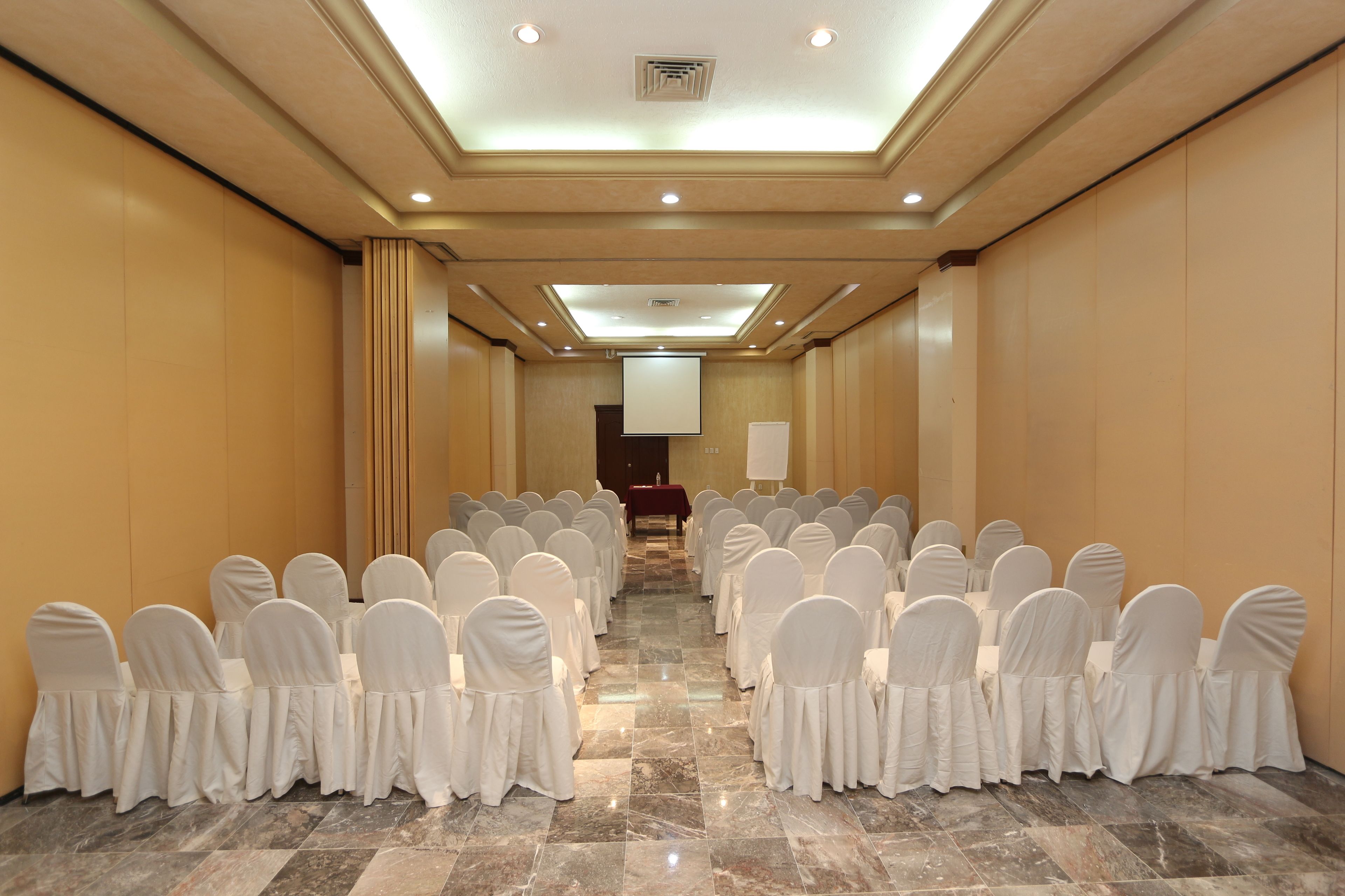 A conference room with rows of white-covered chairs facing a podium at the front.