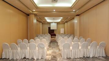 A conference room with rows of white-covered chairs facing a podium at the front.