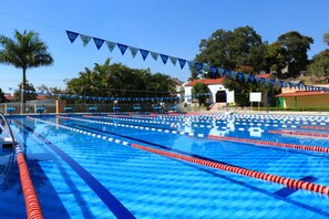 Une piscine avec plusieurs couloirs de nage, un espace de repos couvert et des palmiers en arrière-plan.
