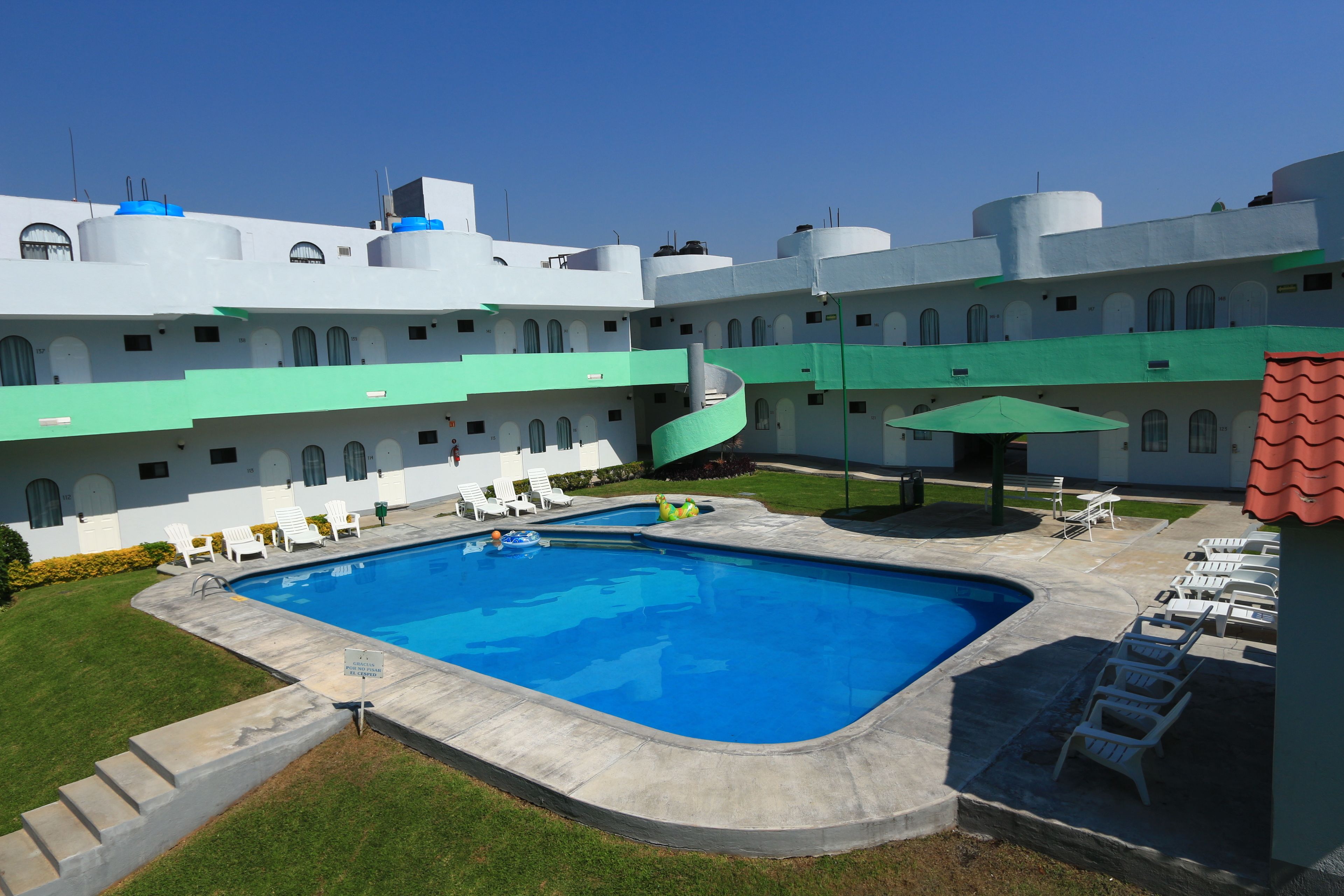 A swimming pool with a spiral slide, surrounded by white buildings with green roofs and multiple balconies.