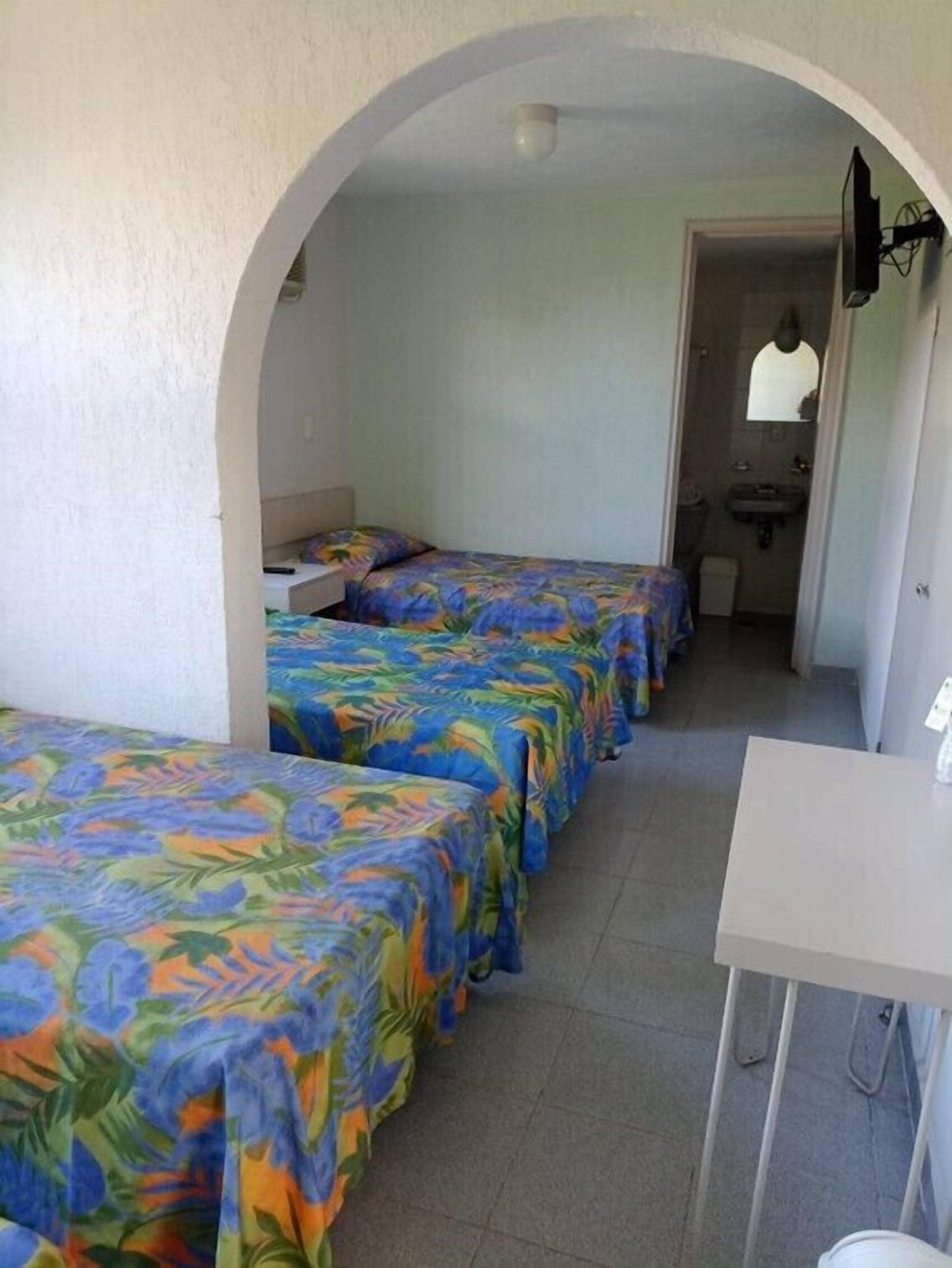 A room with three beds, a desk, and a bathroom visible through an archway.