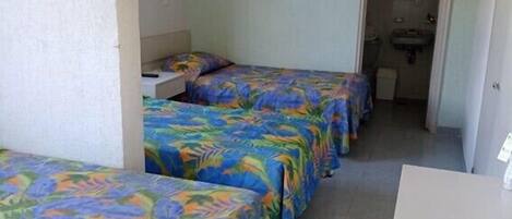 A room with three beds, a desk, and a bathroom visible through an archway.