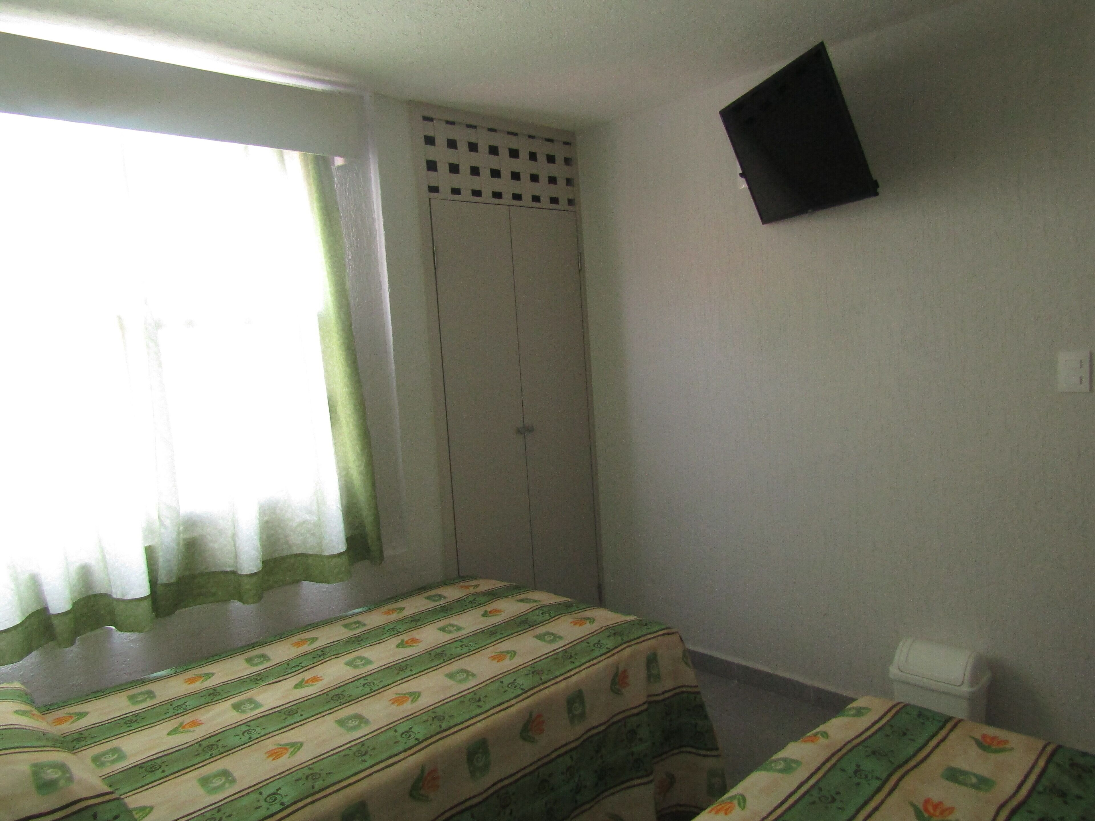 A bedroom with a bed, a wardrobe, a television mounted on the wall, and a window with curtains.