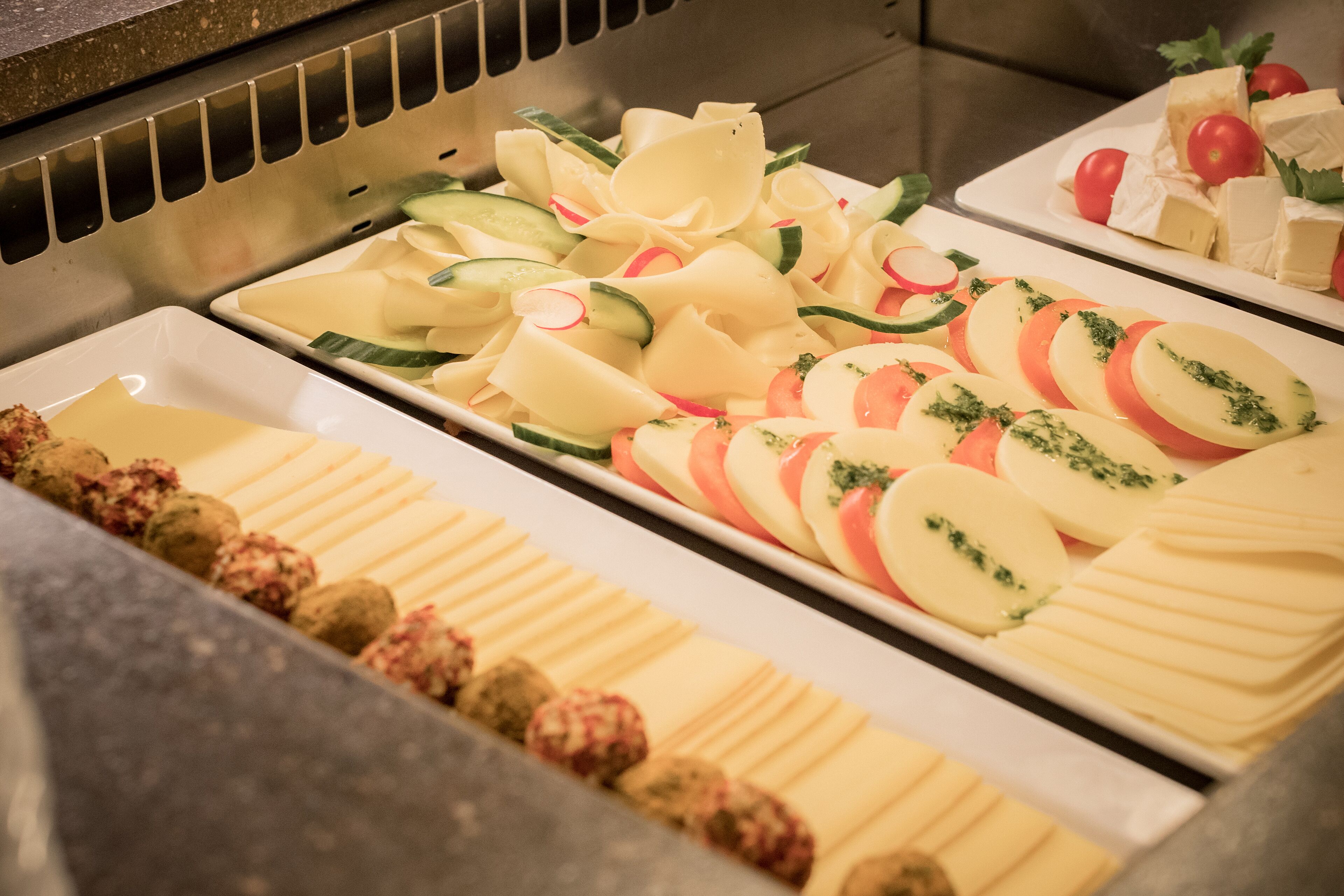 A buffet with various food items including sliced vegetables, cheese, and meatballs.