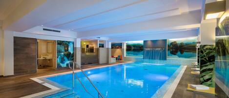 Una piscina interior con agua cristalina, un trampolín y una zona de recepción con vistas a la piscina.