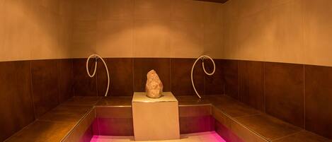 Een spa ruimte met een centraal stenen element, twee gebogen douchekoppen en een roze verlichte vloer.