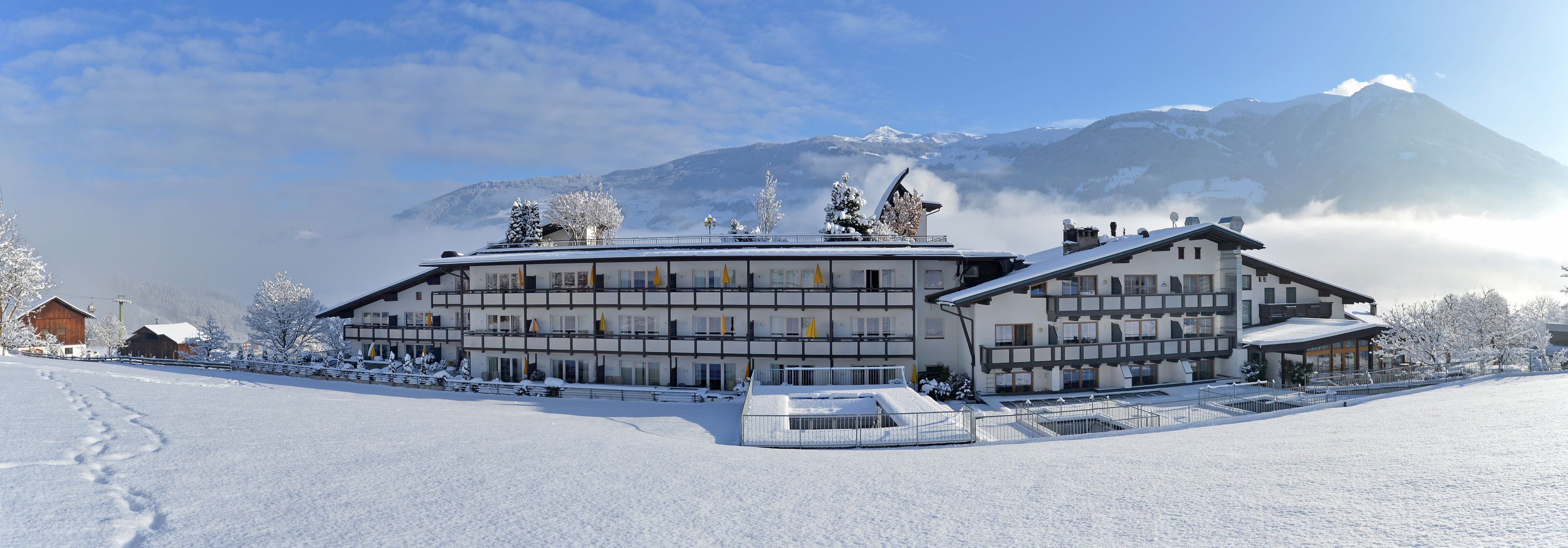 Un hotel de varios pisos con un telesilla, rodeado de árboles nevados y montañas.