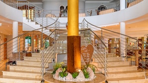 Un espacioso vestíbulo de hotel con un atrio central, varios niveles y una imponente escalera.