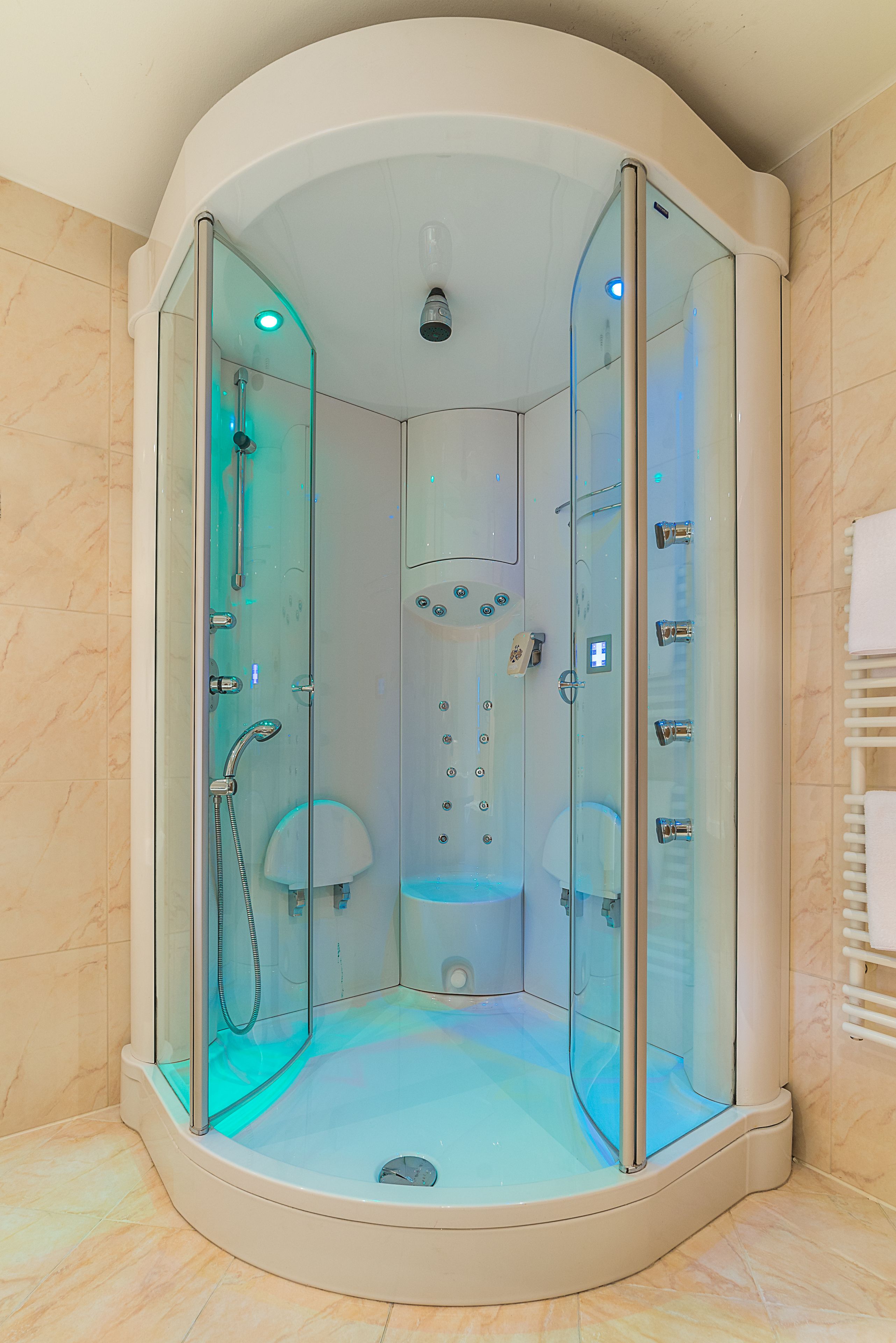 A glass-enclosed walk-in shower with a control panel, a handheld showerhead, and a handheld scrubber.