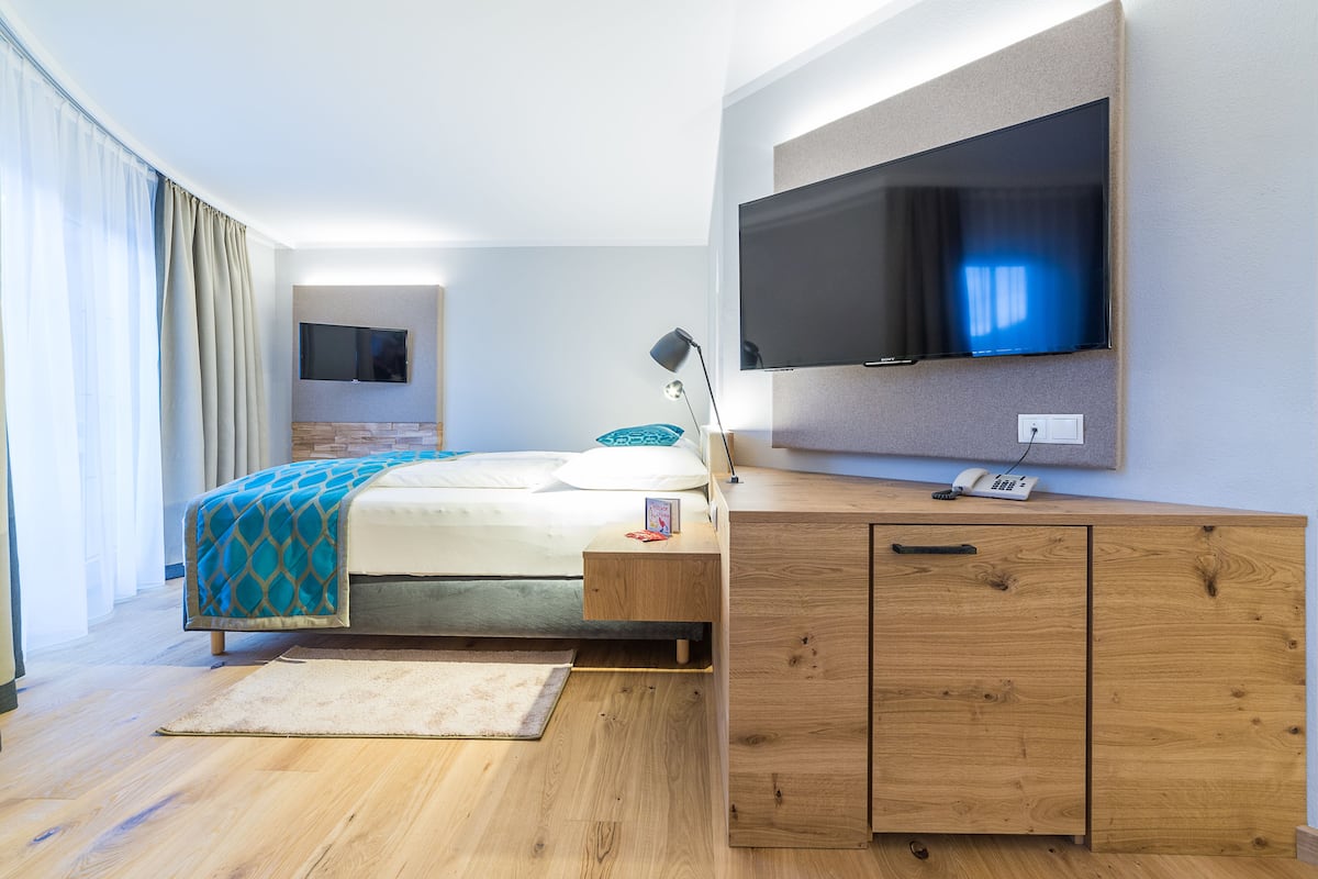 A modern hotel room with a bed, a desk, a flat-screen TV, and a large window with curtains.
