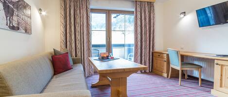 A room with a wooden table, a sofa, a chair, a TV, and a window with curtains.