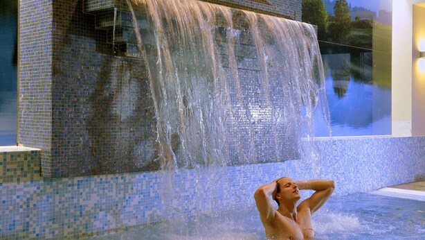 Una persona en una piscina con una cascada al fondo.