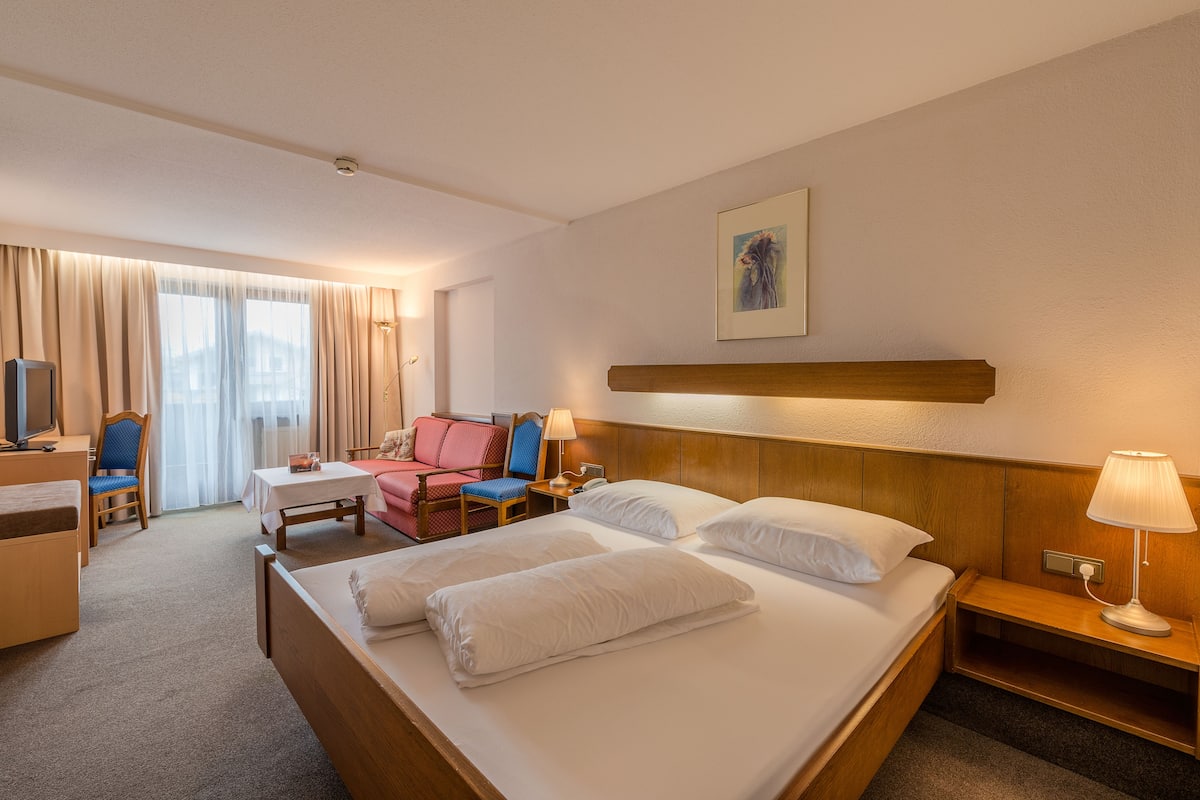 A hotel room with a large bed, a desk with a chair, a small table, and a TV.