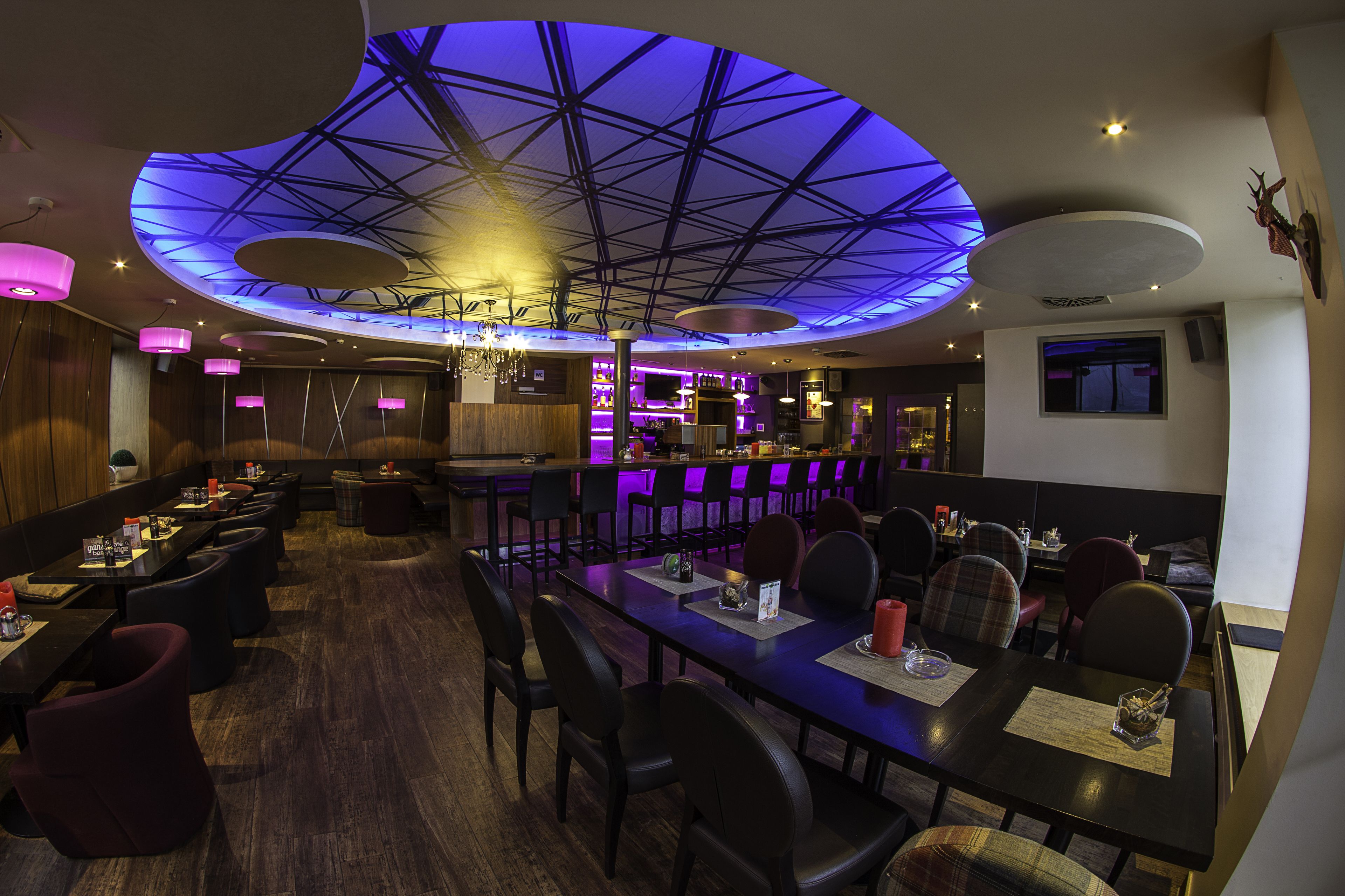 A restaurant with a modern interior, featuring a unique ceiling design and a bar area.