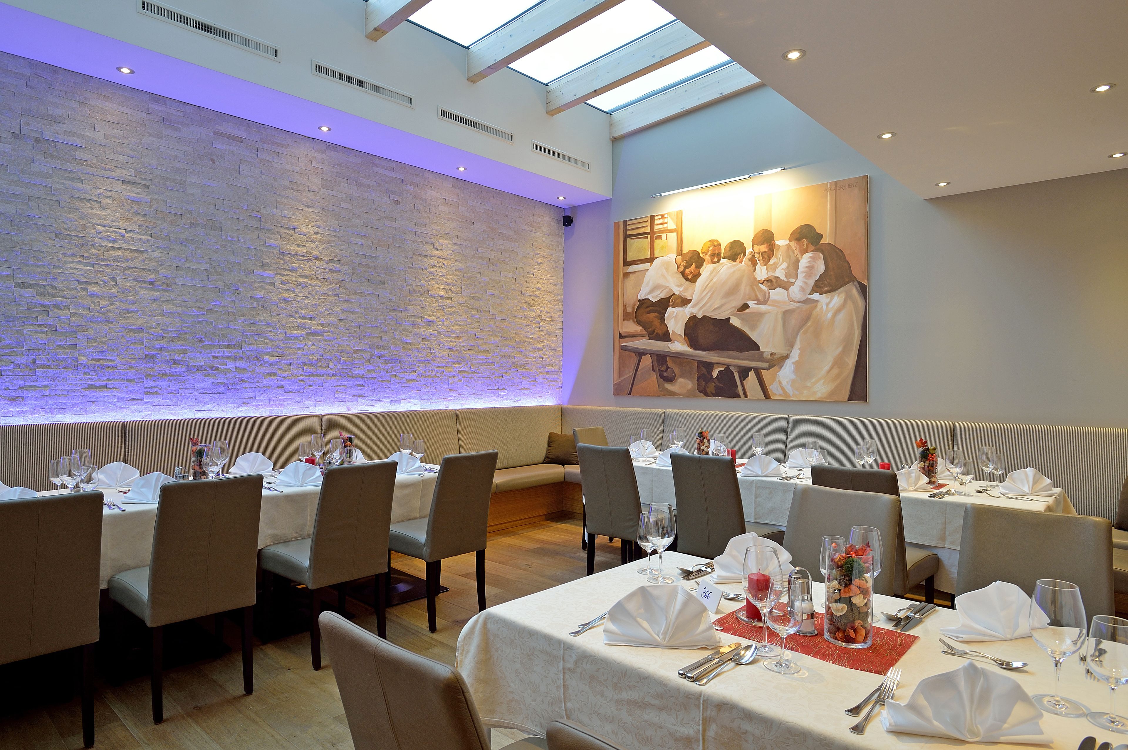 A restaurant with multiple tables set for dining, a stone wall, and a large painting on the wall.