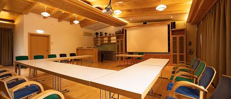 Una sala de conferencias con una larga mesa, varias sillas, una pantalla de proyector y vigas de madera en el techo.