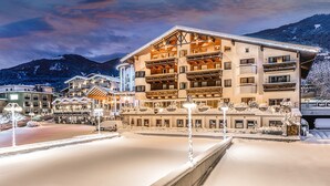 Un hotel de varios pisos con balcones, suelo cubierto de nieve y montañas al fondo.