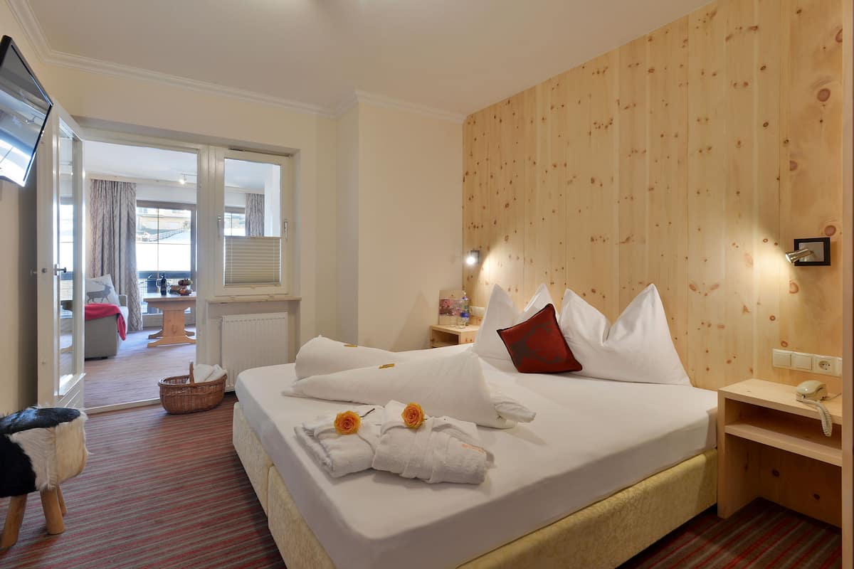 A hotel room with a large bed, a wooden headboard, a bedside table with a lamp, and a television mounted on the wall.