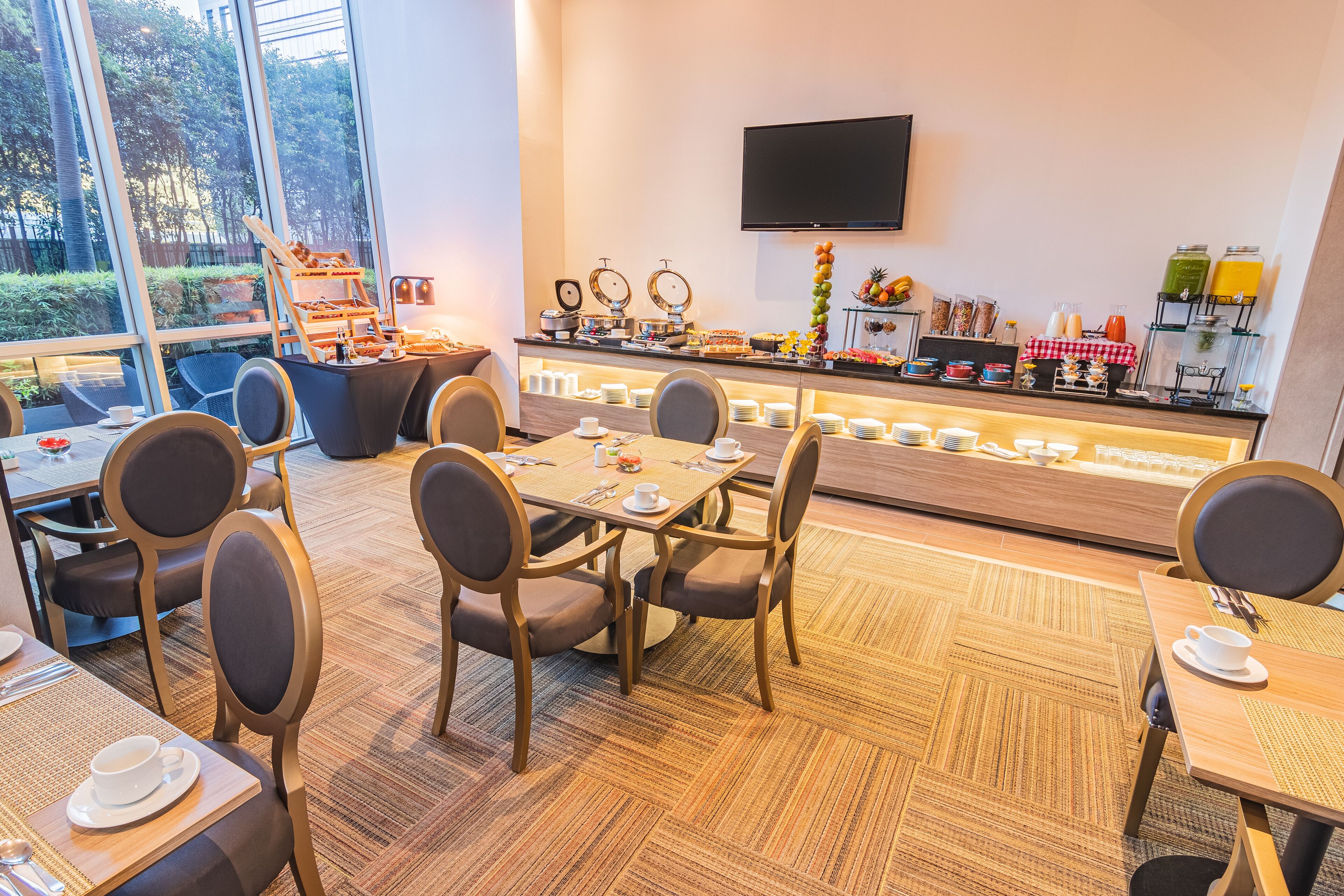 Ein Frühstücksbereich eines Hotels mit Tischen, Stühlen, einem Buffet und einem Fernseher an der Wand.