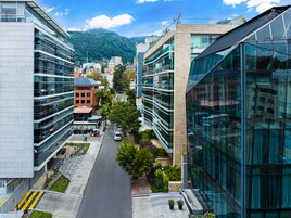 A modern urban street with contemporary buildings, a clear sky, and a mountain in the background.