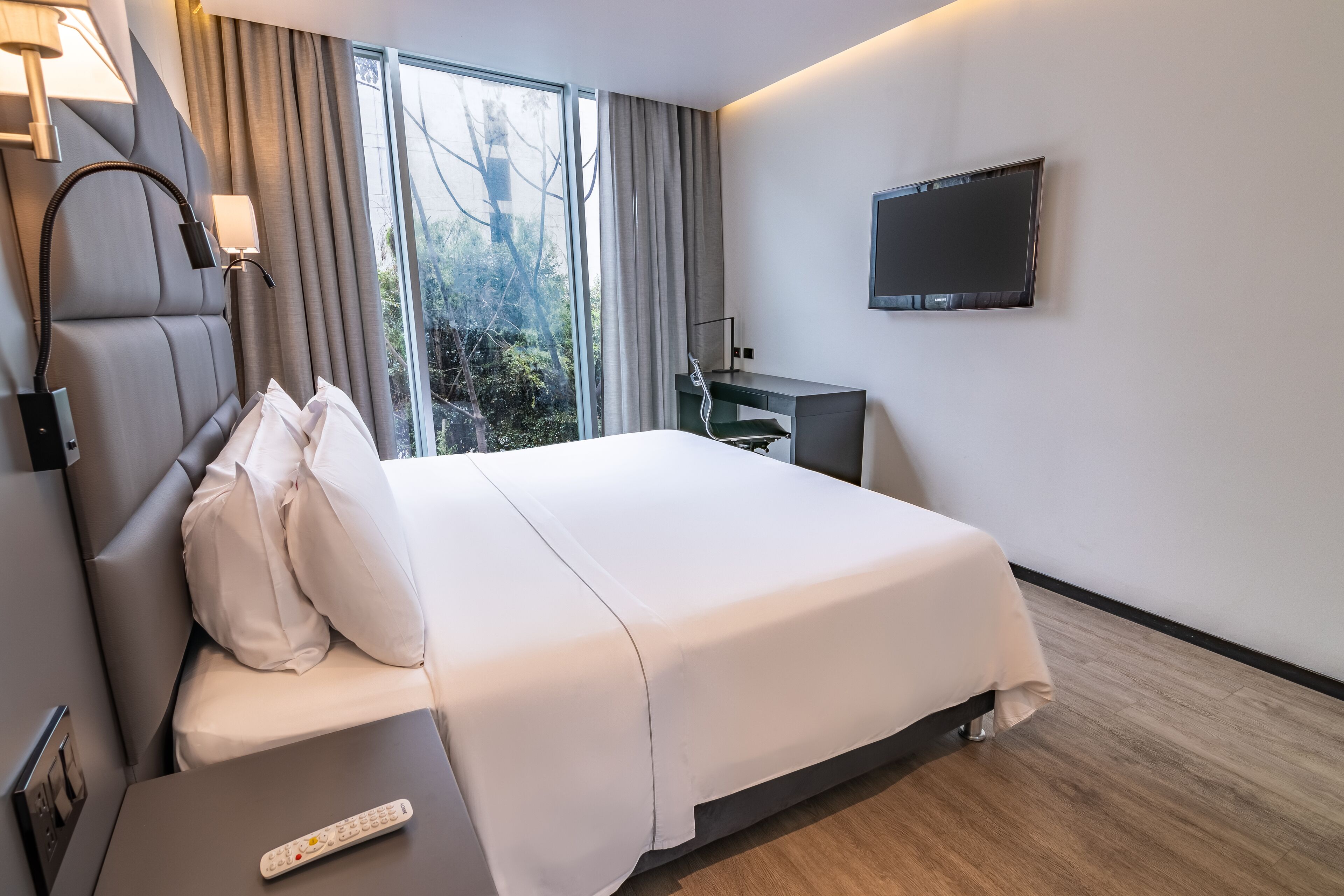 A hotel room with a bed, a desk, a TV, and a window with curtains.