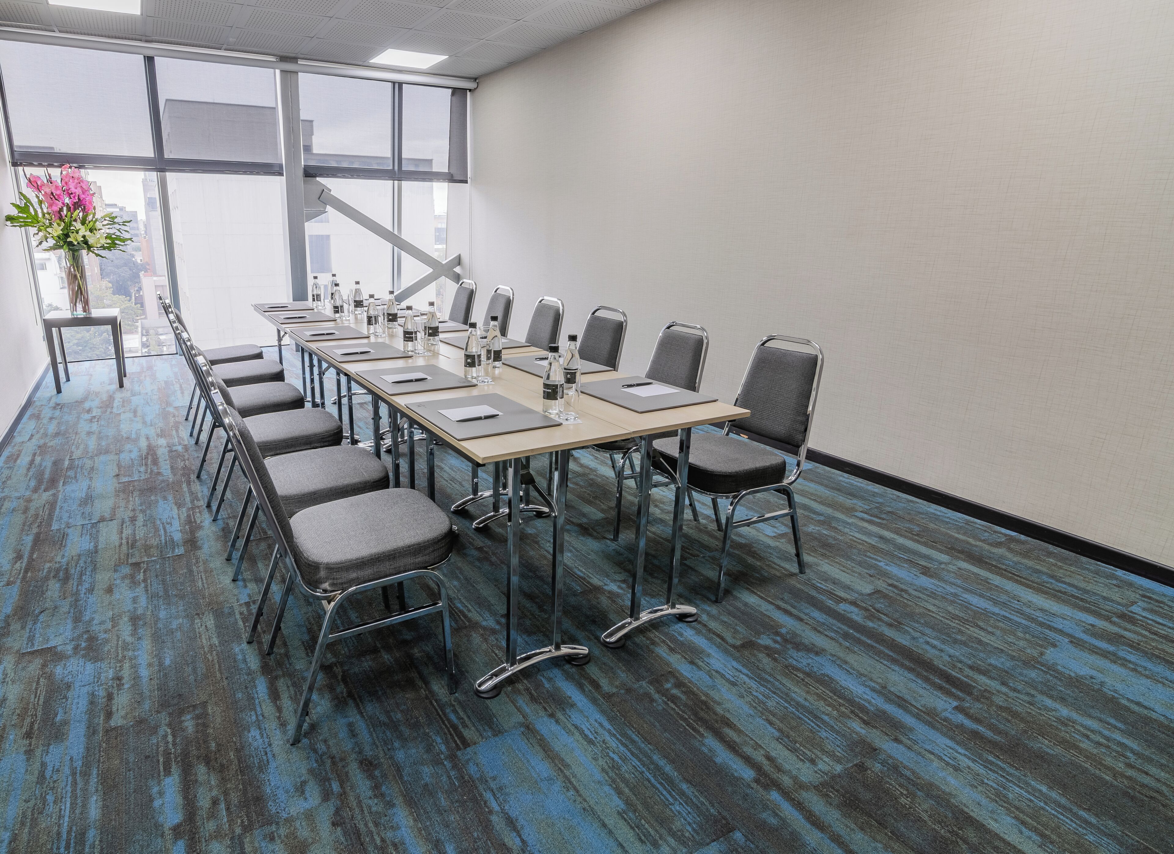 A conference room with a long table, chairs, and a vase of flowers.