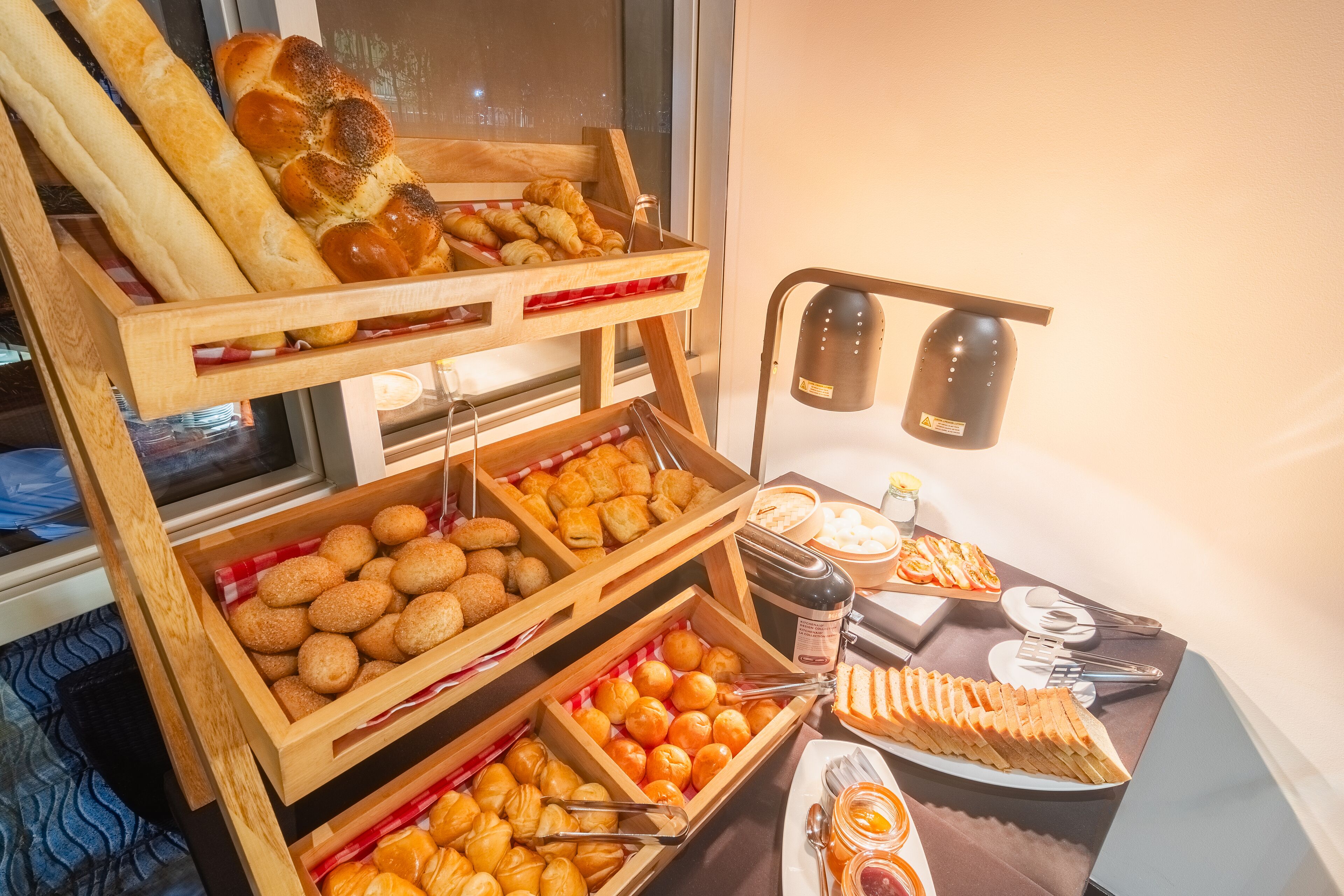 A buffet with various baked goods and pastries, including bread, croissants, and muffins, arranged on wooden stands.