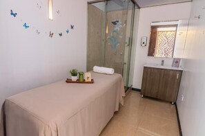 A room with a massage table, a small cabinet, a decorative mirror, and butterfly wall decals. - Hotel GHL Collection 93 (Bogotá)