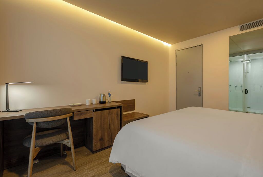 Une chambre d’hôtel avec un lit, un bureau, une chaise, une télévision et une porte.