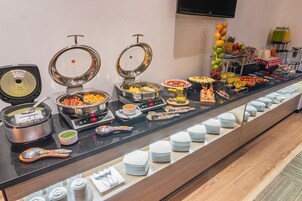 Monipuolinen buffet, jossa on tarjolla erilaisia ruokia ja juomia, kuten kahvi ja hedelmävalikoima.