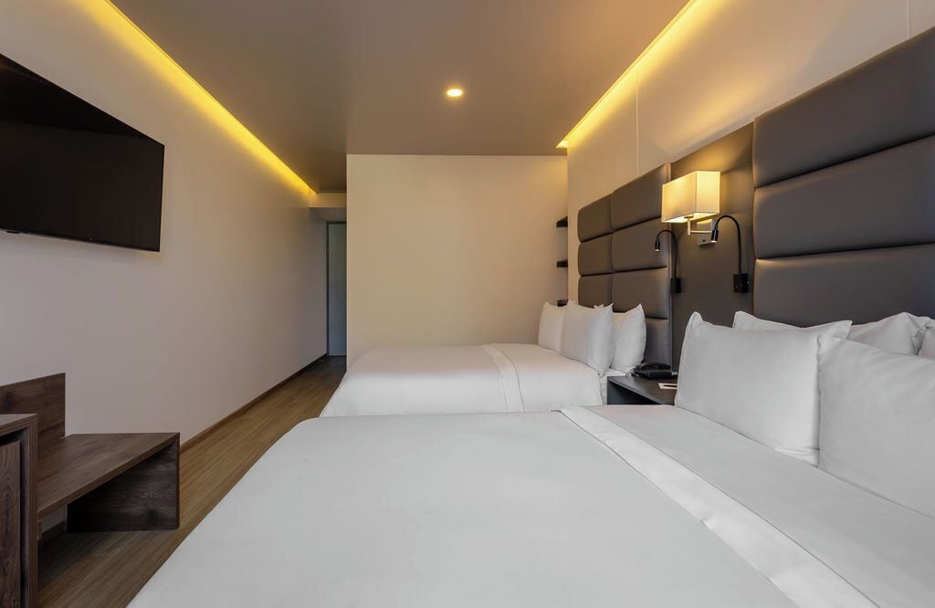 A hotel room with a large bed, a smaller bed, a desk, and a TV mounted on the wall.
