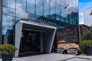 Collection Hotel 93 -hotellin ulkopuoli: moderni lasijulkisivu, tiiliseinä ja kaksi mustaa tuolia etualalla.