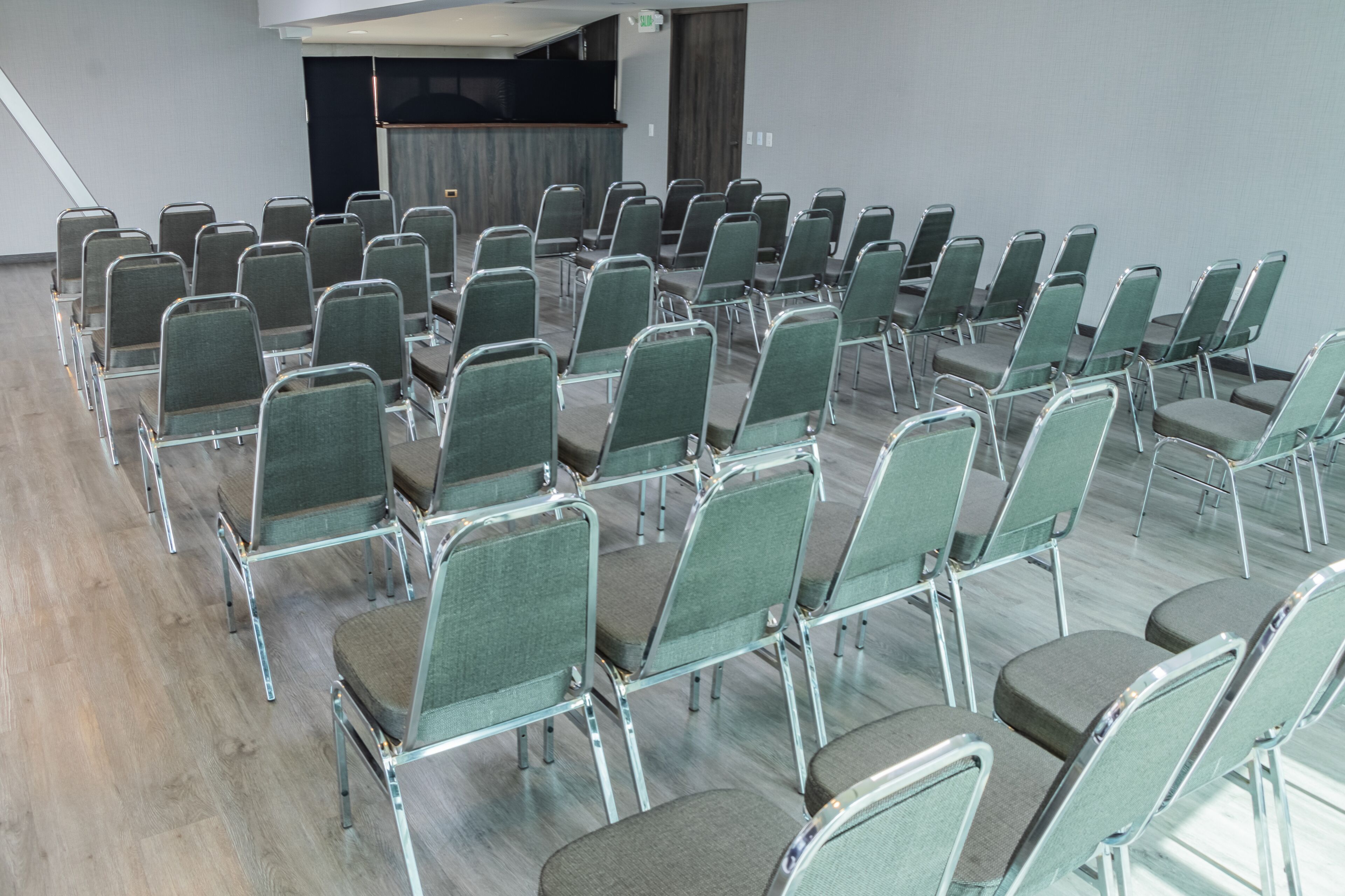 Un salón de conferencias con filas de sillas verdes y suelo de madera.