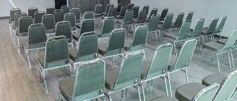Un salón de conferencias con filas de sillas verdes y suelo de madera.