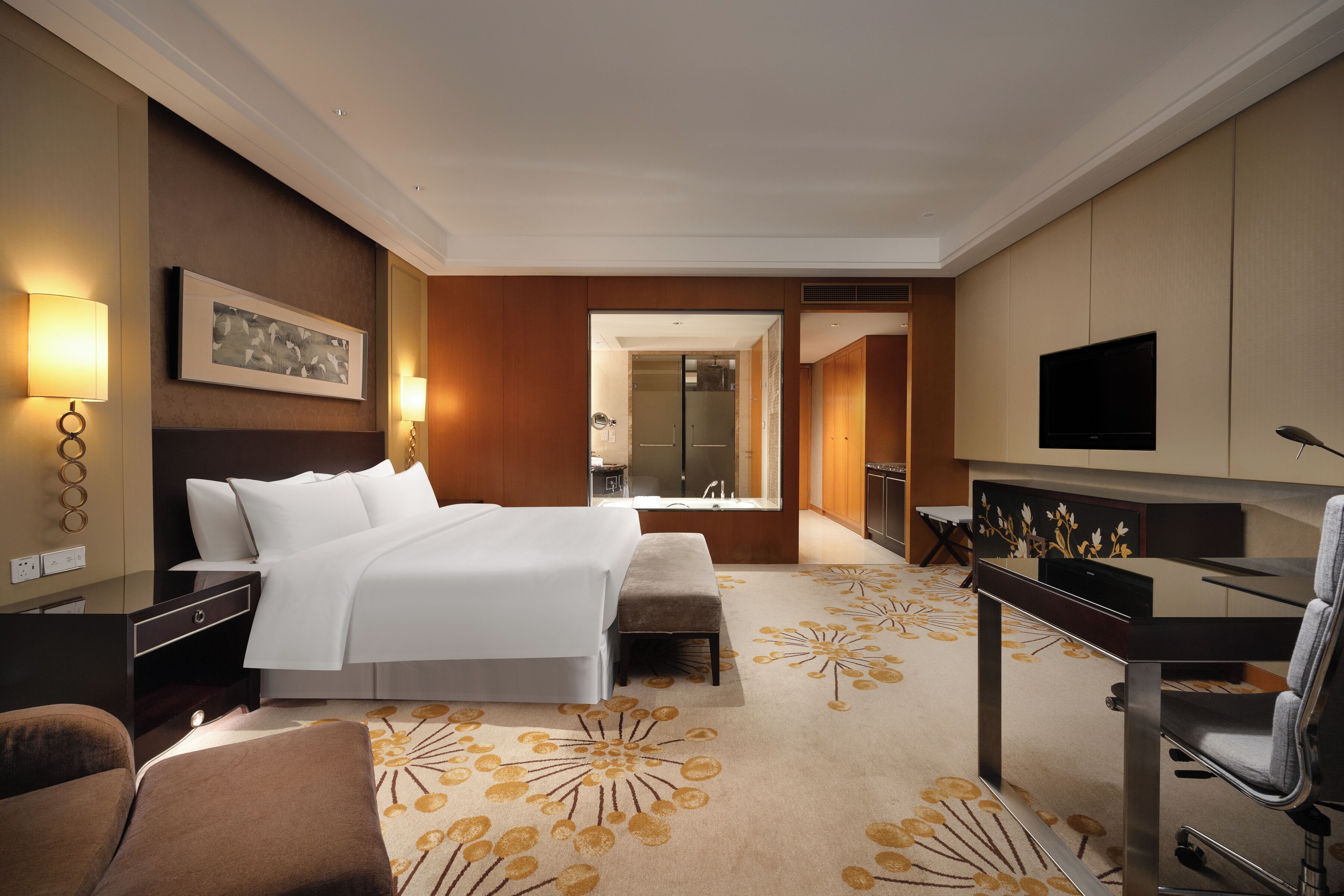 Habitación de hotel con cama, mesitas de noche, escritorio con silla, televisión y baño visible a través de una puerta abierta.