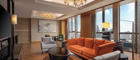 A modern living room with a large orange sofa, grey armchairs, a glass coffee table, and a chandelier.