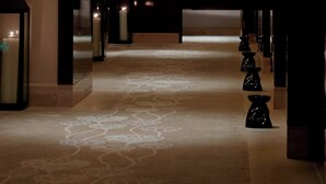 A hallway with a patterned carpet, a decorative tree artwork, and a series of black vases along the wall.