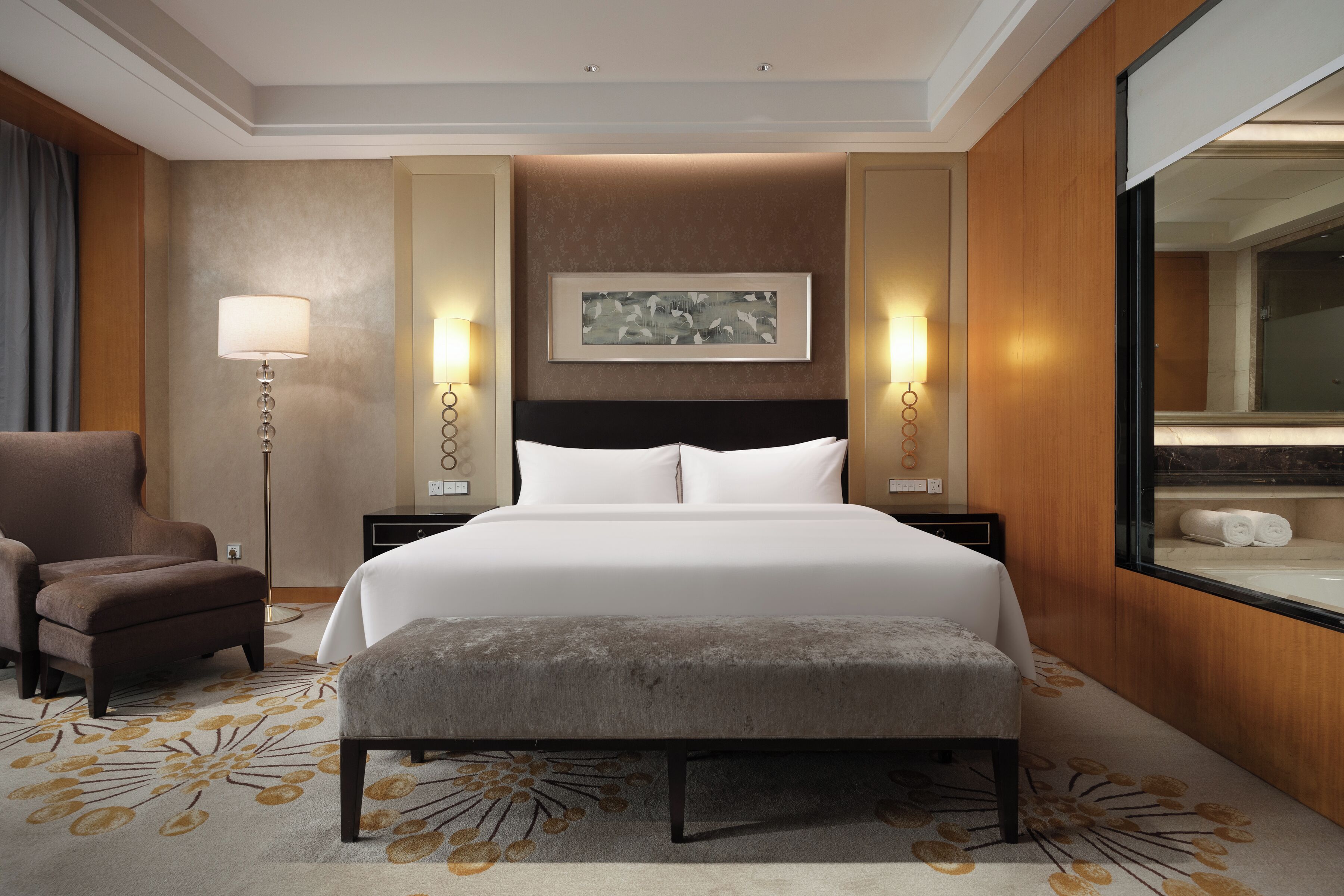 Een hotelkamer met een groot bed, een stoel, een vloerlamp en een schilderij aan de muur.