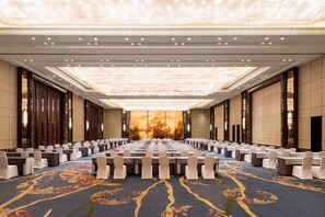 A conference room with rows of tables and chairs, a patterned carpet, and a large chandelier.