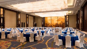 A banquet hall with round tables, white chairs, and a large chandelier.