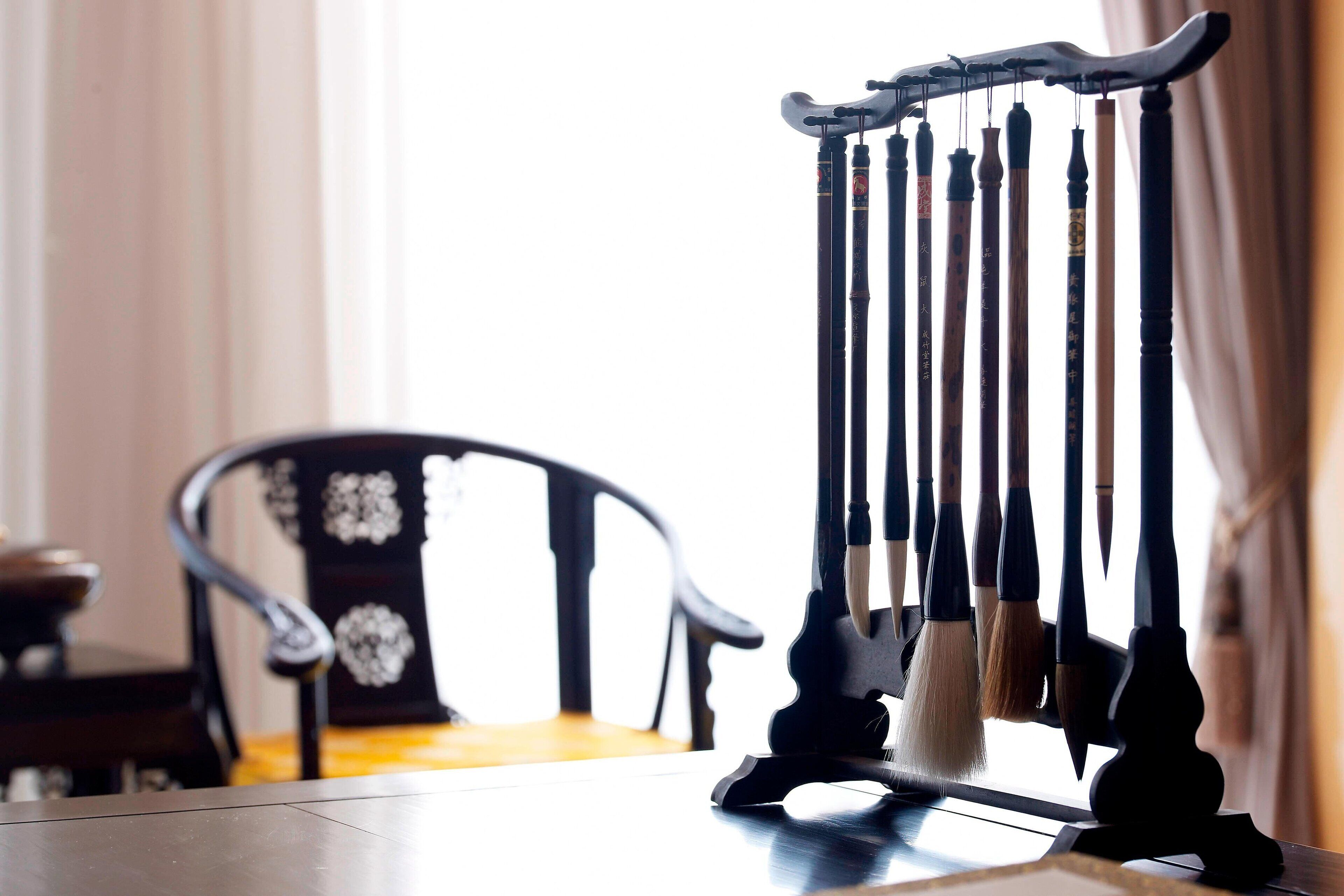 Un juego de pinceles chinos tradicionales sobre un soporte, una silla negra con motivos florales y una mesa.