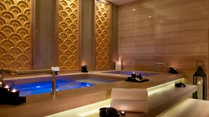 A spa area with two hot tubs, wooden benches, candles, and a modern design.