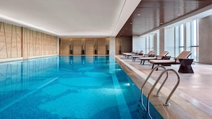 An indoor swimming pool with clear water, wooden panel walls, and lounge chairs along the side.