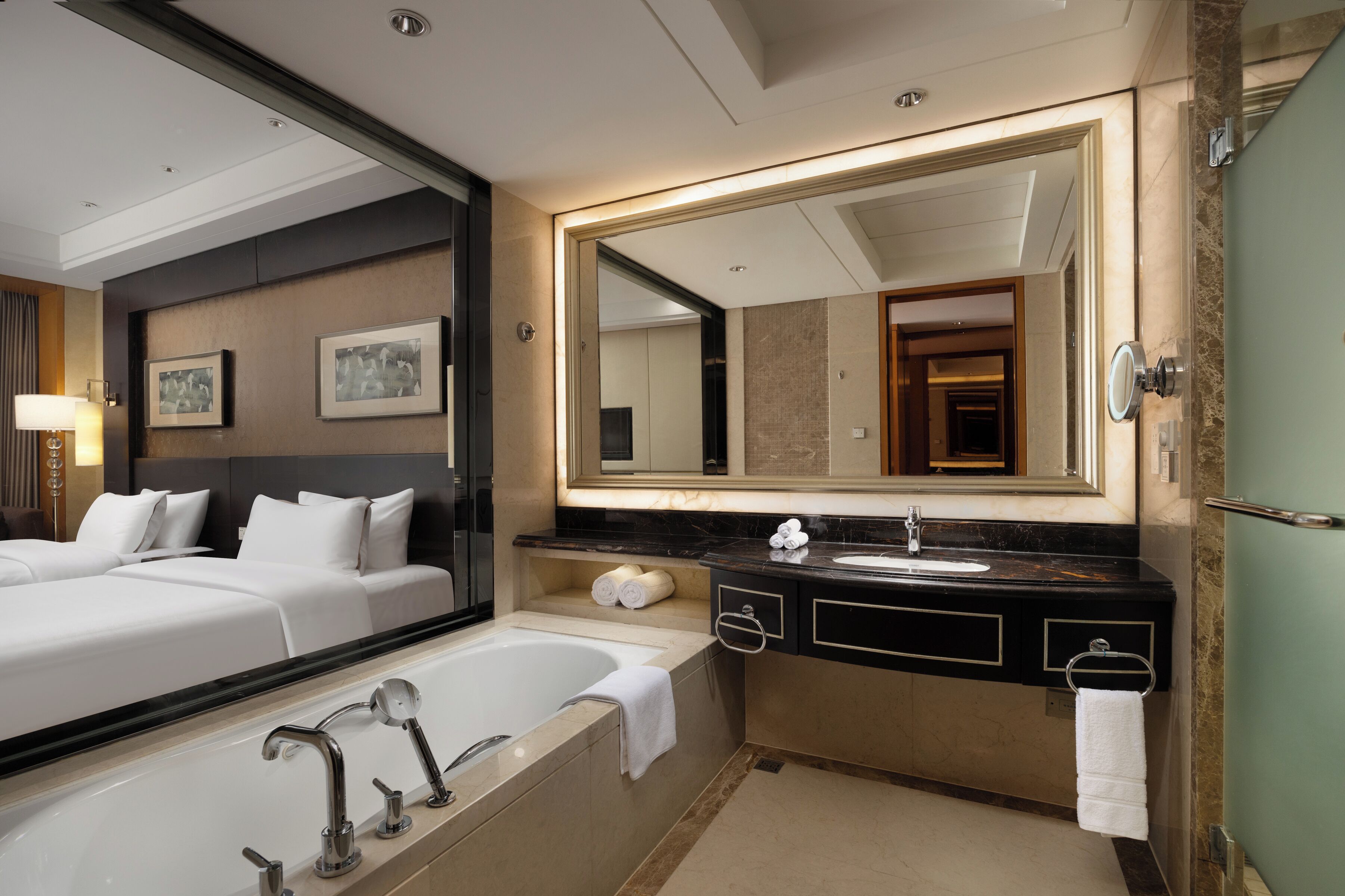 A hotel bathroom with a large mirror, a bathtub, a sink, and a toilet.