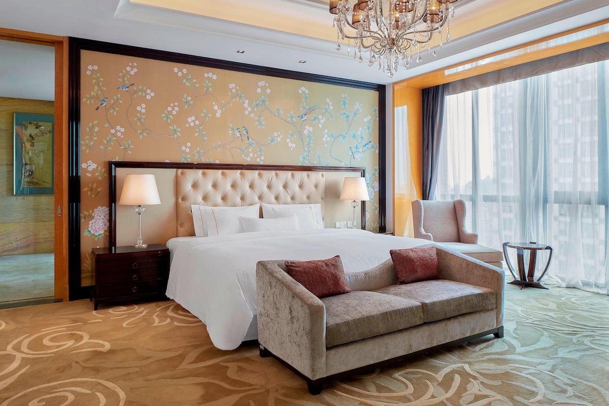 A hotel room with a large bed, two bedside lamps, a sofa, and a chandelier.