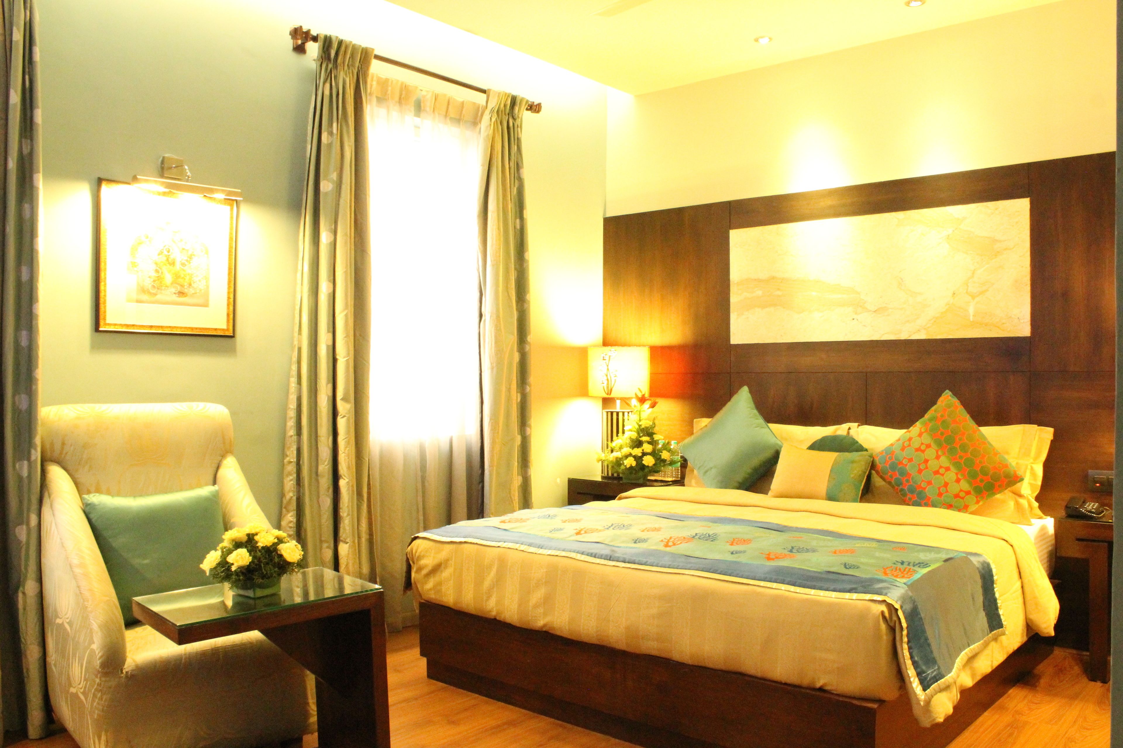 A hotel room with a bed, a chair, a nightstand, and a wall-mounted picture.