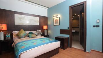 Un dormitorio con una cama grande, dos mesitas de noche, un tocador, una lámpara de pared y una puerta que da a un baño.