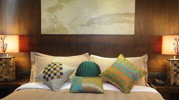 Habitación de hotel con una cama grande, varios almohadones, dos mesitas de noche con lámparas y un cuadro abstracto de gran tamaño en la pared.