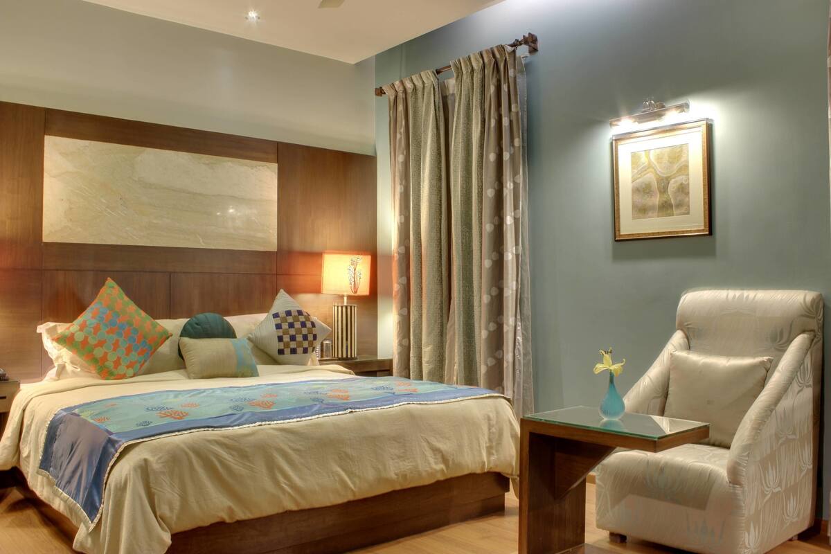 Une chambre d’hôtel avec un lit, une chaise, une table de chevet, une lampe et un tableau au mur.